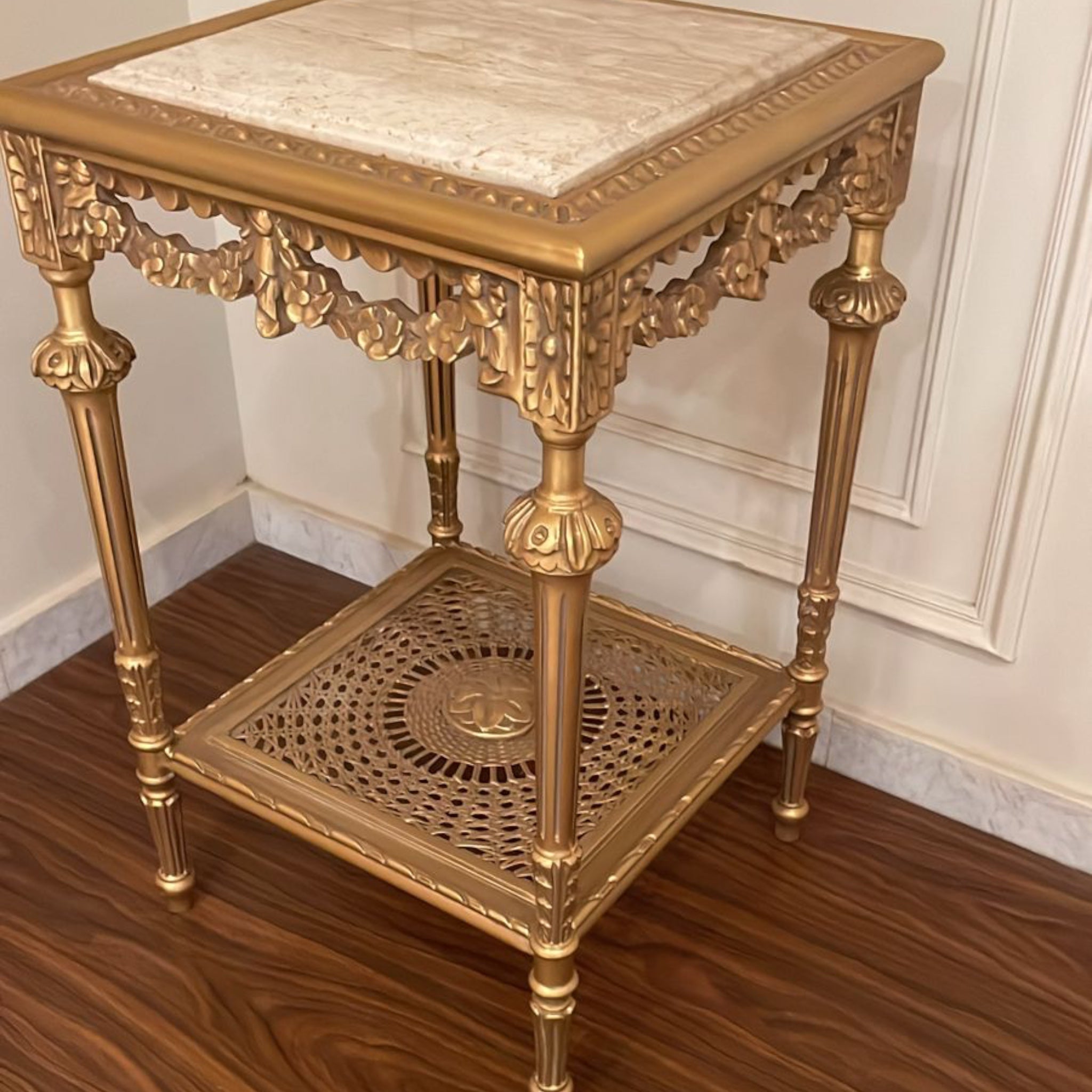 ترابيزة ركن فاخرة بزخارف نحاسية وقرصة رخام - طاولة ركن أنيقة بتصميم كلاسيكي مميز مصنوعة من خشب الزان المتين، مطلية بلون ذهبي فاخر مع زخارف يدوية تضيف لمسة فخامة. القرصة من الرخام الطبيعي، والرف السفلي يتميز بتصميم شبكي مزخرف فني يعزز جمالها ويضيف طابعًا تراثيًا ساحرًا الخاماتالهيكل: خشب زان طبيعيالسطح: رخام طبيعيالرف السفلي: إطار مزخرف بلون ذهبي المقاساتالعرض: 46 سمالارتفاع: 73 سمالعمق: 46 سم